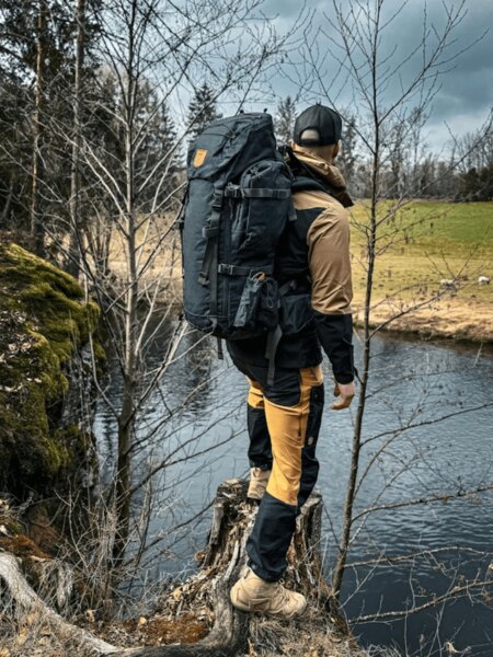 Outdoorové kalhoty Fjällräven a batoh u říčního břehu v přírodě. Foto: Rigad