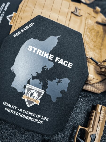 Tvrdý balistický plát se stranou STRIKE FACE (PGD); v pozadí plate carrier a služební pistole, detail před vložením do nosiče.