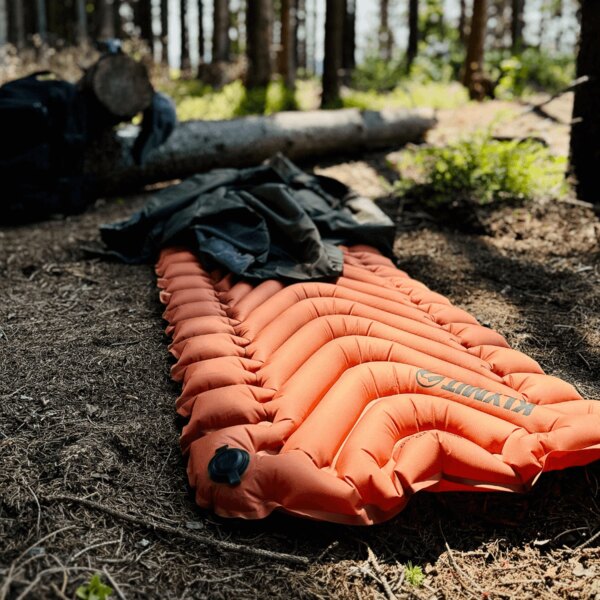 Zateplená nafukovací karimatka Static V™ Klymit® oranžová v lese. Foto: Rigad