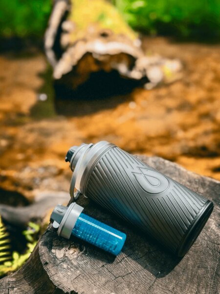 Láhev Flux HydraPak s filtrem Cap položená na pařezu v přírodě, ideální na cestování a outdoor. Foto: Rigad