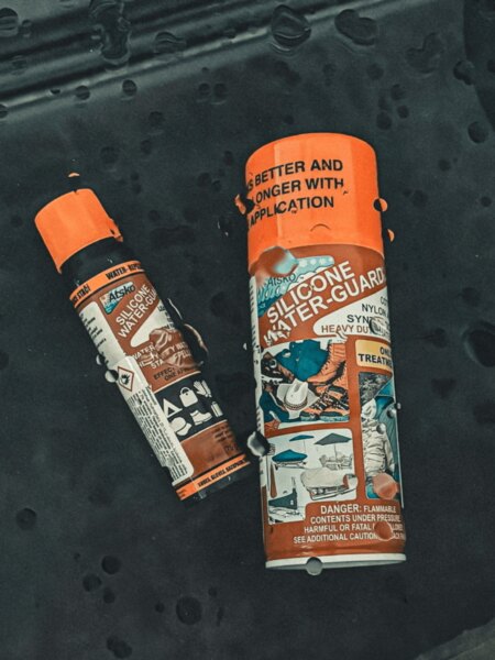 Impregnační spreje Atsko Silicone Water-Guard položené na tmavé tkanině s kapkami vody.