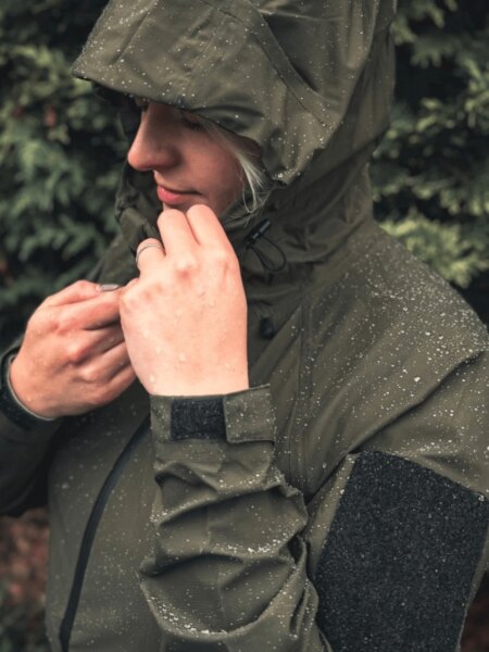 Žena v nepromokavé bundě Helikon-Tex Squall s kapkami vody na kapuci a rukávech.