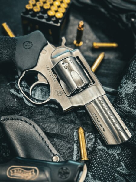 Revolver Ruger GP100 v ráži .357 Magnum položený vedle nábojů a střeleckého pouzdra.