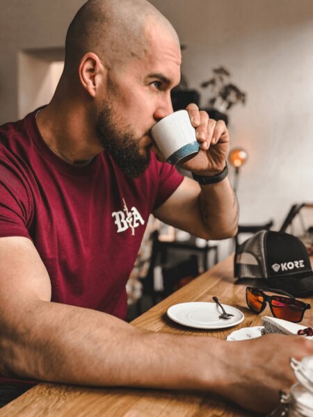 Muž s taktickým vzhledem u kávy – detail na tričko BfA a čepici Kore Essentials. Foto: Rigad