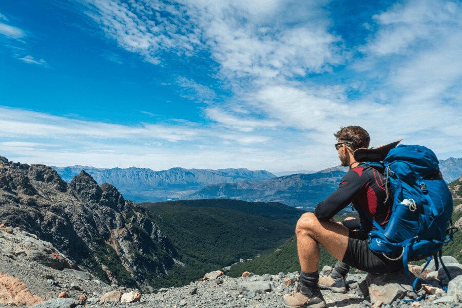 Muž sedící na skále s batohem a funkčním oblečením, pozorující horskou krajinu. Foto: https://www.pexels.com/cs-cz/foto/krajina-hory-priroda-muz-15954827/