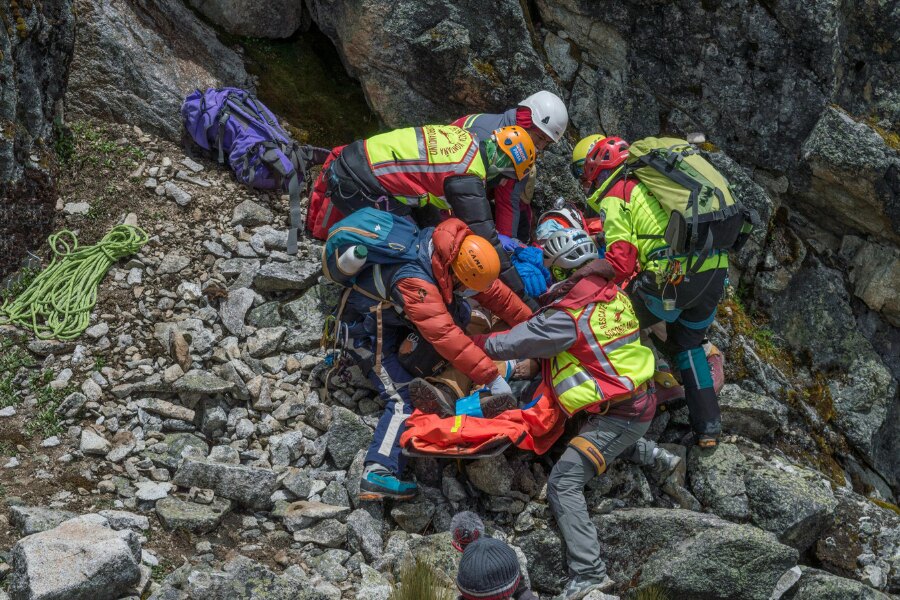 Horské záchranné družstvo stabilizuje zraněného během evakuace v kamenitém terénu. Foto: https://www.pexels.com/cs-cz/foto/skupina-zachranaru-zachranujicich-zranenou-osobu-na-rocky-mountainside-9424563/