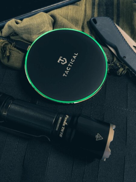 Bezdrátová nabíječka Base Plug Tactical® s rozsvíceným LED kroužkem položená na taktickém vybavení – Qi 15 W, protiskluzový povrch. Foto: Rigad