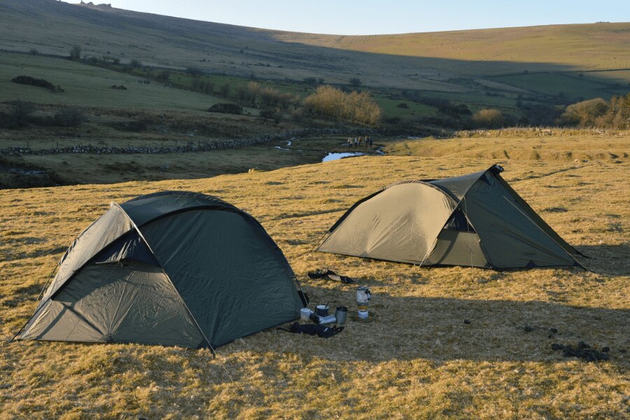 Dva trekové stany postavené na louce pod horským hřebenem při podzimním táboření. Foto: Rigad