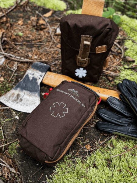 Lékárnička Helikon-Tex Bushcraft Medical Kit v hnědém pouzdře, položená v lese u sekerky a rukavic – lékárnička pro bushcraft a outdoor. Foto: Rigad.