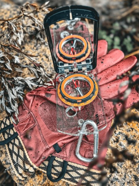Kompas a rukavice položené v terénu – navigace v přírodě bez GPS pomocí buzoly. Foto: Rigad