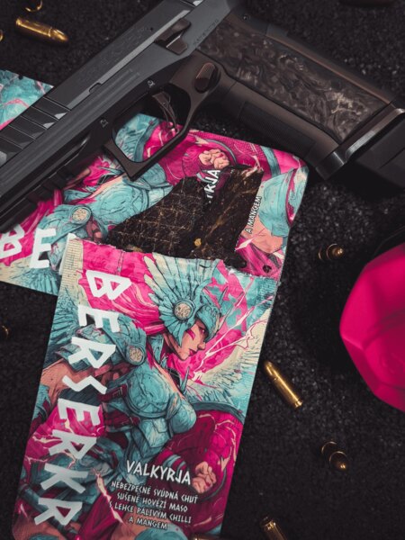 Balení sušeného masa Berserkr VALKYRJA Mango a Chilli s viditelným kouskem jerky, umístěné vedle zbraně a střeliva. Foto: Rigad