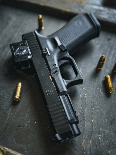 Glock 47 s kolimátorem Aimpoint COA na A-CUT, detail pistole s náboji na stole, Foto: Rigad