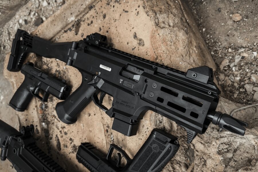 Moderní samopal CZ Scorpion EVO 3 s kolimátorem a teleskopickou pažbou položený na zemi vedle pistolí a zásobníků. Foto: Rigad