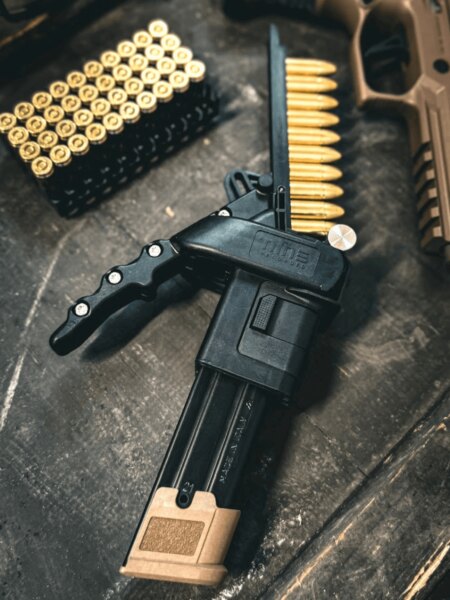 Nabíječ zásobníků Nine Reloaded vedle nábojů ráže 9 mm Luger a pistole.