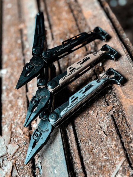 Tři multitooly Leatherman Signal v různých barevných provedeních položené na dřevěném povrchu.