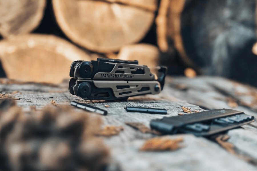 Leatherman Signal položený na dřevěném stole s bity a příslušenstvím v outdoorovém prostředí.
