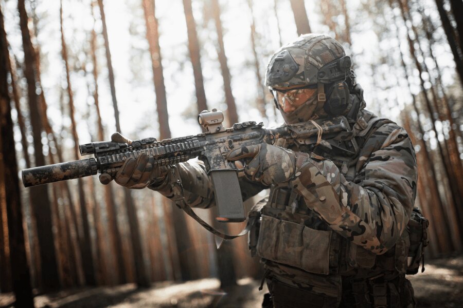 Moderní puška AR-15 s kolimátorem a tlumičem při střelbě v lesním prostředí.