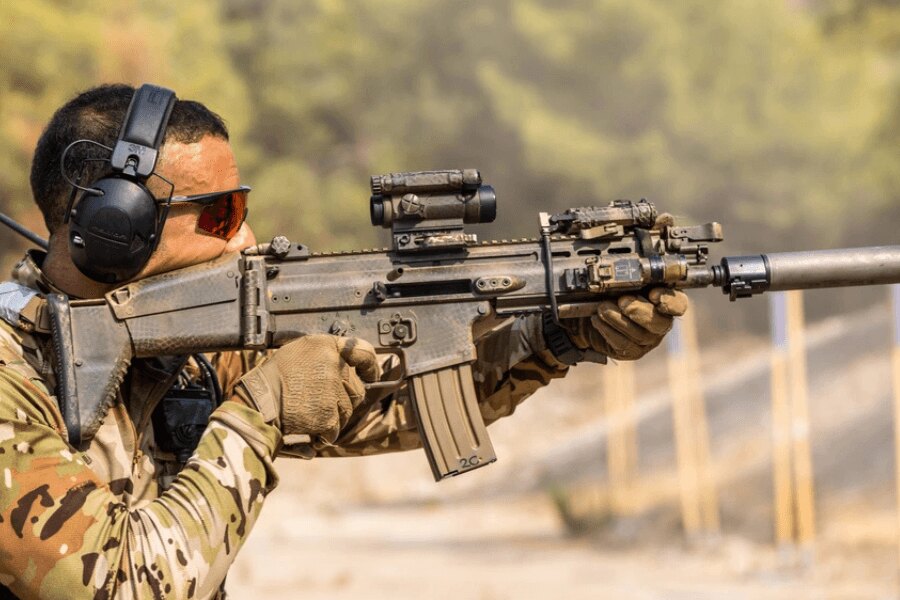Střelec s puškou FN SCAR vybavenou kolimátorem, svítilnou a tlumičem.