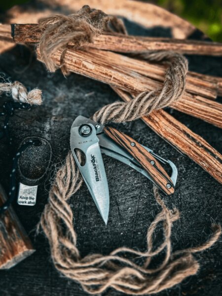 Zavírací nůž BlackFox s dřevěnými střenkami položený na špalku vedle podpalového dřeva.