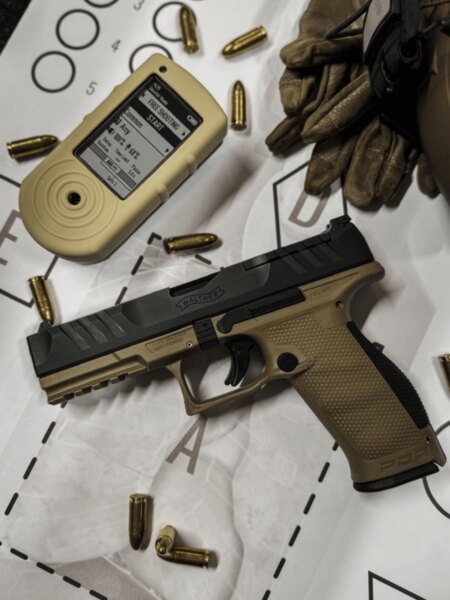 Pistole Walther PDP Full Size se střeleckým timerem, náboji a rukavicemi položená na terči.