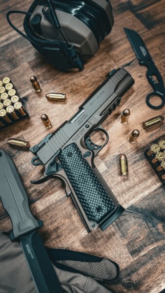 Pistole Schmeisser HUGO 1911 5" v ráži .45 ACP položená na stole se střelivem a střeleckým vybavením.