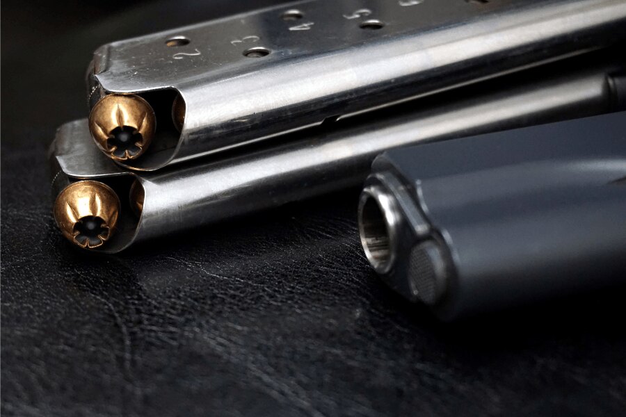Detail zásobníků pistole M1911 s náboji .45 ACP a částí pistole v pozadí.