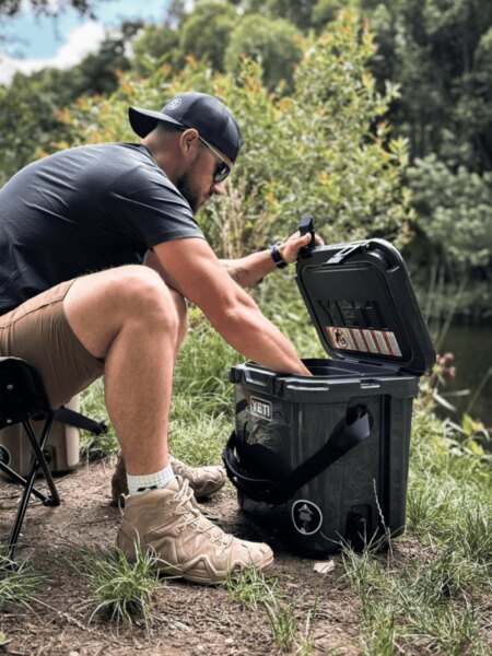 Muž otevírá transportní box YETI LoadOut GoBox při pobytu u vody.
