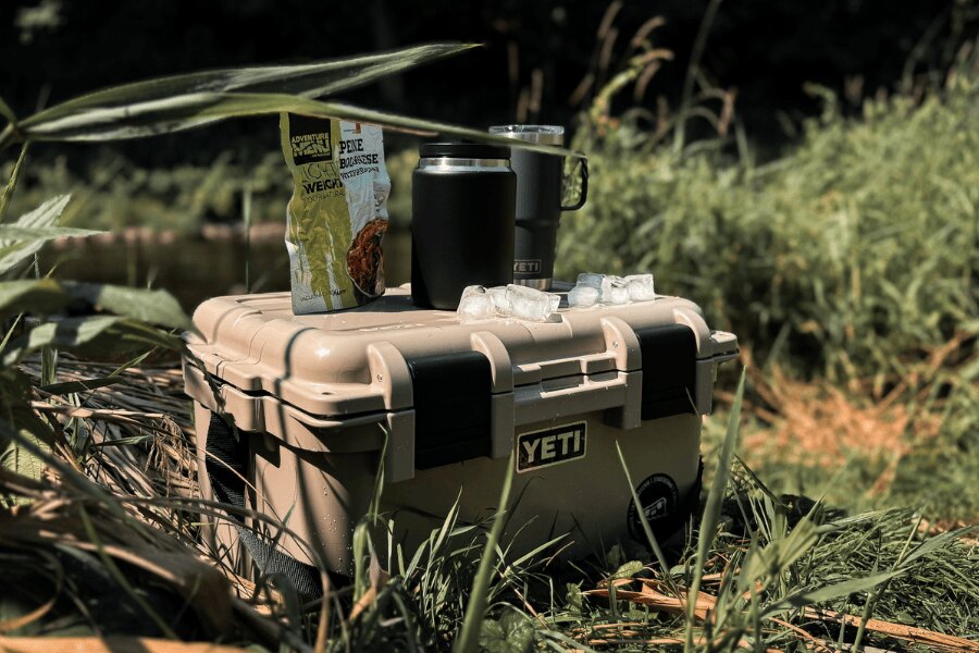 Transportní box YETI LoadOut GoBox s baleným jídlem a termohrnky v přírodě.
