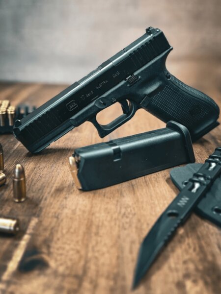 Pistole Glock 17 Gen5 s mechanickými mířidly položená na stole se zásobníkem, střelivem a nožem.