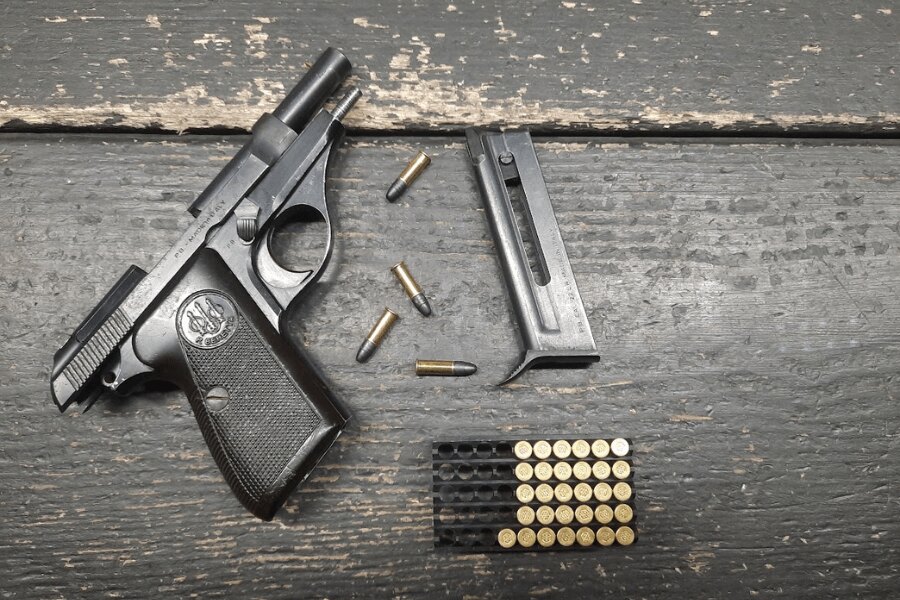 Pistole Beretta 71 s vyjmutým zásobníkem a náboji .22 LR na tmavém dřevěném stole.