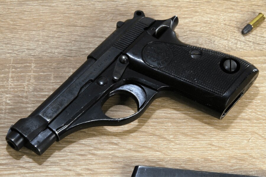 Detail pistole Beretta 71 položené na světlém dřevěném stole.