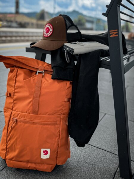 Oranžový batoh Fjällräven High Coast Foldsack 24 opřený o lavičku