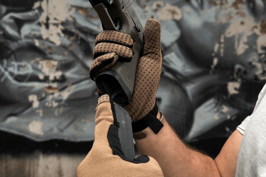 Detail dlaní rukavic Bivoj Dýlejc s protiskluzovými pryžovými kolečky při manipulaci s pistolí.