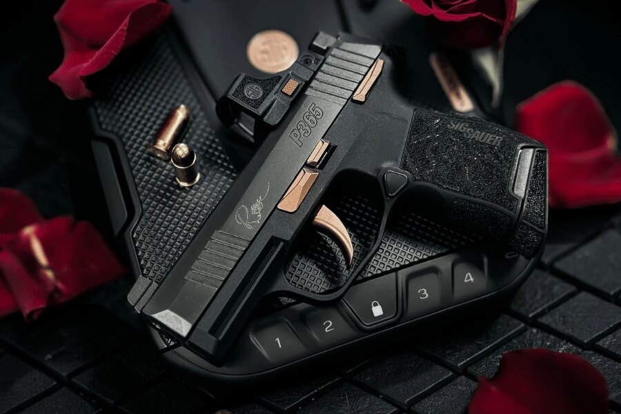 Pistole SIG Sauer P365 ROSE s kolimátorem a růžově zlatými prvky na uzamykatelném boxu mezi okvětními lístky růží.