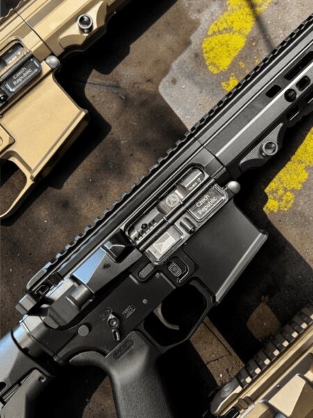 Tři pušky platformy AR-15 v černém a pískovém provedení položené vedle sebe na betonovém povrchu.