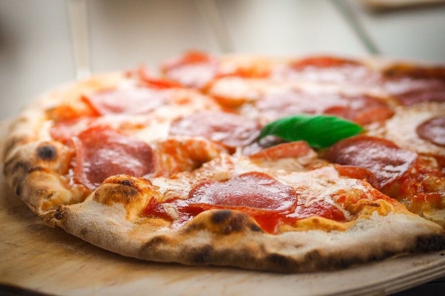 Salámová pizza na dřevěném talíři.